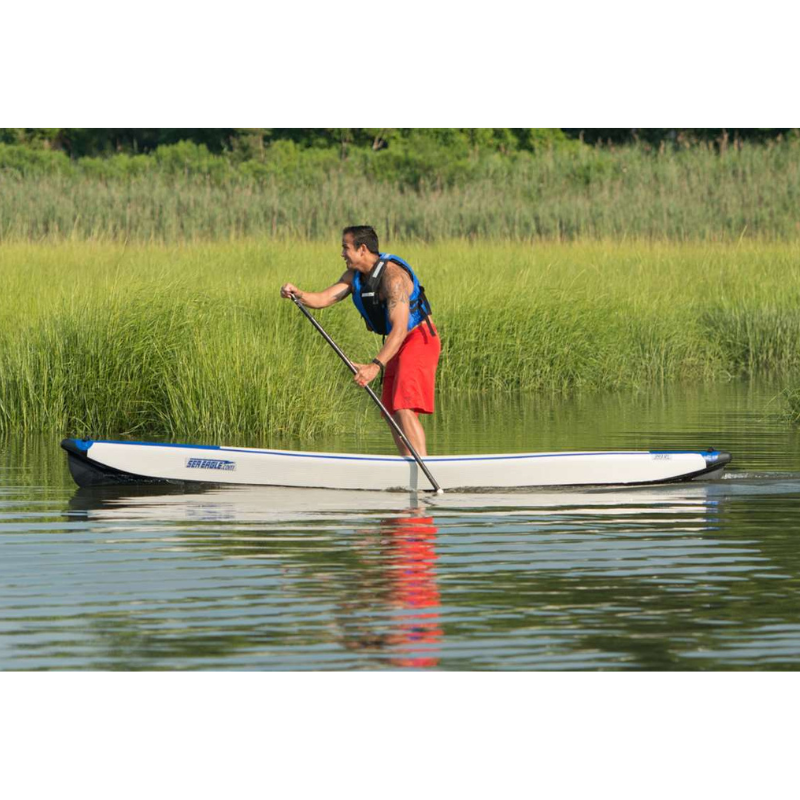 Sea Eagle RazorLite 393RL Inflatable Kayak Person paddleboarding on a calm body of water with grassy bank in the background