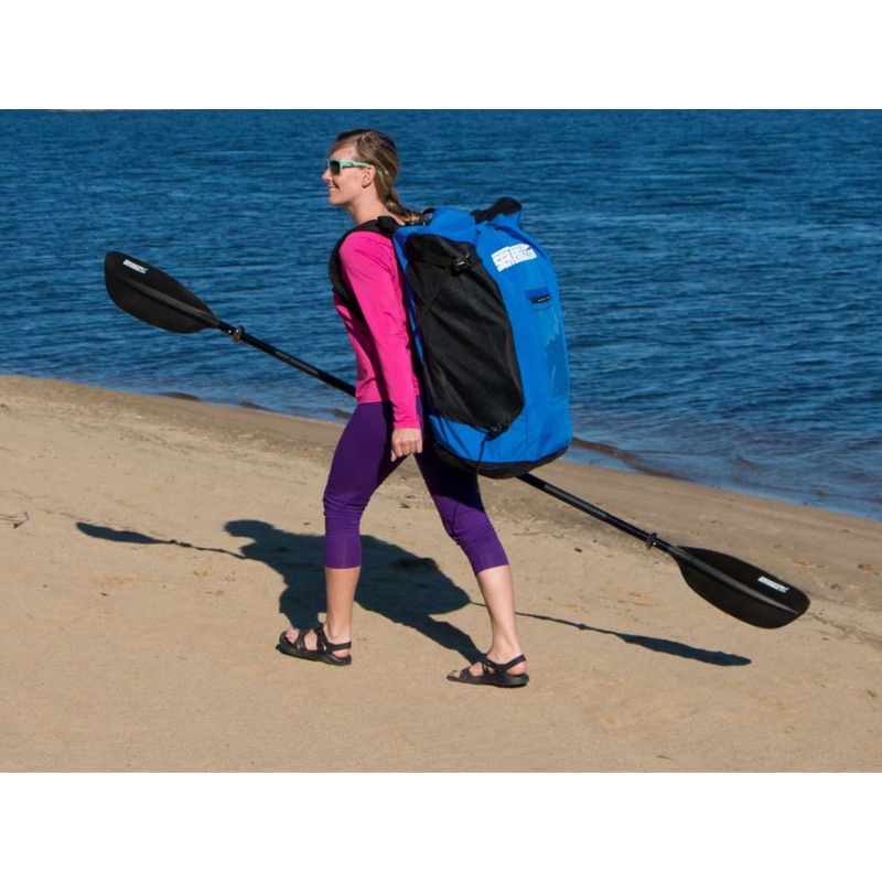 Sea Eagle RazorLite 393RL Inflatable Kayak Person carrying a blue kayak backpack and paddle on a beach.